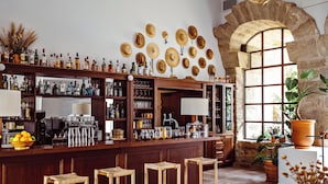 Een bar met houten krukken, flessenrekken vol drank en een stenen boog met een raam.