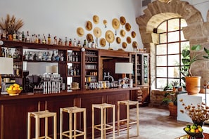 Un espace bar avec des tabourets, des étagères remplies de bouteilles et une arche en pierre.