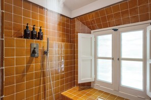 A bathroom with brown tiled walls, a shower, a white door, and a window. - Le Moulin (Lourmarin)