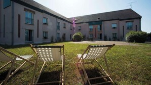 A courtyard with two lounge chairs and a building with multiple windows and balconies. - Brit Hotel Nogent Le Rotrou Hotel Du Perche (Nogent-le-Rotrou)