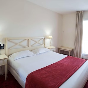 Ein Hotelzimmer mit einem Bett, Nachttischen, einer Lampe, einem Telefon und einem Fenster mit Vorhängen.