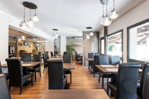 A modern restaurant with wooden tables and black chairs, pendant lighting, and large windows. - Hotel La Cle Des Champs (Claix)