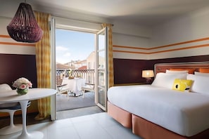 Ein Hotelzimmer mit Bett, Tisch mit Blumenvase, einer Pendelleuchte und Blick ins Freie.