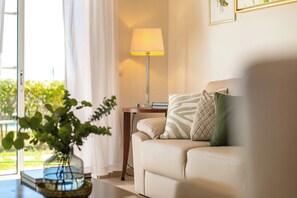 A living room with a sofa, a lamp, a vase with plants, and a view of greenery outside. - Monte Da Poupa - 7 bedroom villa - Sleeps 14 (Albufeira)