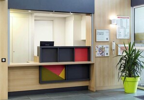 A reception desk with a digital screen, a potted plant, and a wall-mounted sign. - B&B Hotel Evry Lisses 3 Etoiles (Lisses)