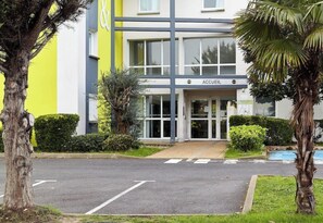 A building with a sign reading 'ACCUEIL' at the entrance, surrounded by greenery and a clear road. - B&B Hotel Evry Lisses 3 Etoiles (Lisses)