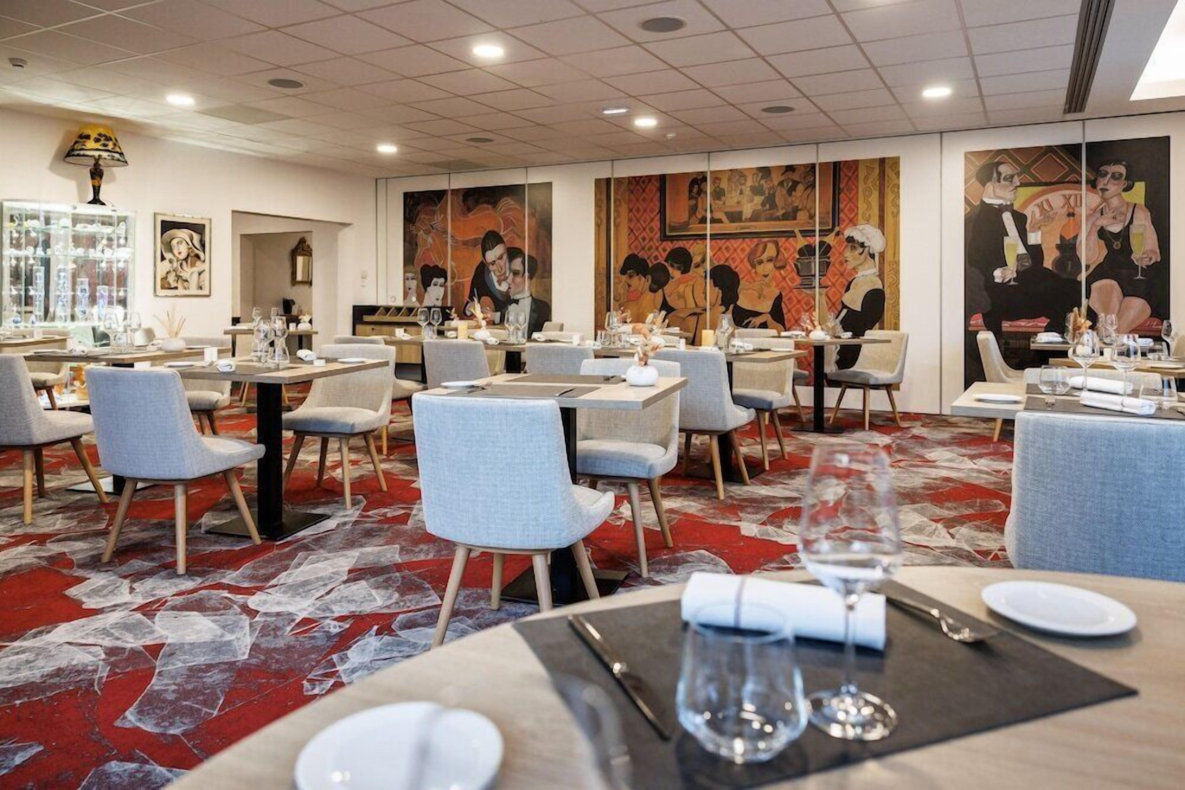 A restaurant with tables set for dining, featuring artwork on the walls and a patterned carpet.