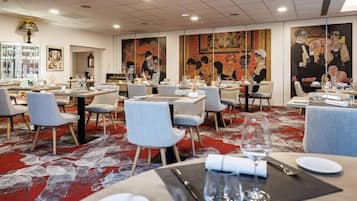 A restaurant with tables set for dining, featuring artwork on the walls and a patterned carpet.