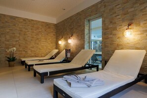 A spa room with three sunbeds, a stone wall, and a window. - Hotel Husseren Les Chateaux (Husseren-les-Chateaux)
