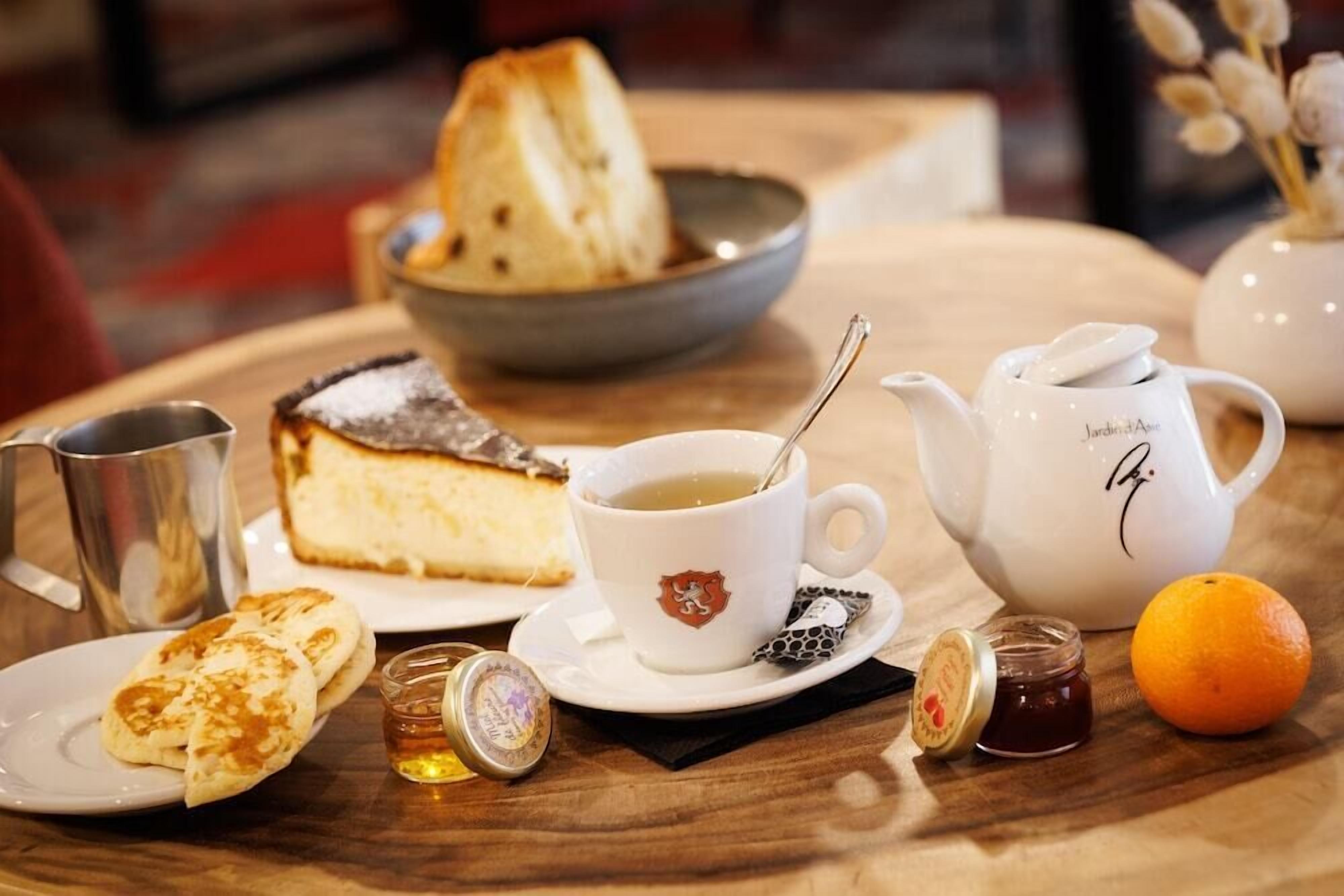 A table with a dessert, a cup of tea, a teapot, a jug, a plate with pastries, a jar of jam, and an orange.