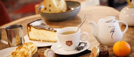 A table with a dessert, a cup of tea, a teapot, a jug, a plate with pastries, a jar of jam, and an orange.