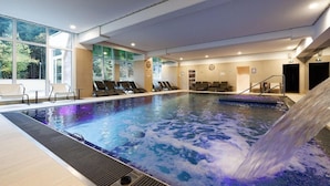 An indoor swimming pool with a waterfall feature, multiple lounge chairs, and large windows offering views of the outdoors. - Hotel Husseren Les Chateaux (Husseren-les-Chateaux)