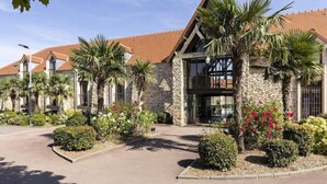 Un hotel con arquitectura de piedra y madera, palmeras y parterres de flores.