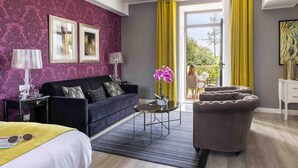 Una habitación de hotel moderna con una pared de diseño morado, un sofá azul oscuro, una mesa de centro redonda y un sillón gris.