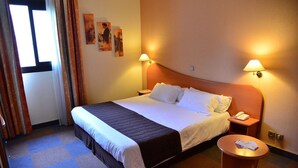 Une chambre d’hôtel avec un lit, des tables de chevet, une table ronde et des lampes fixées au mur.