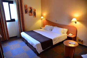 A hotel room with a bed, bedside tables, a round table, and wall-mounted lamps. - Aeroport Hotel - Parc Expo (Mauguio)