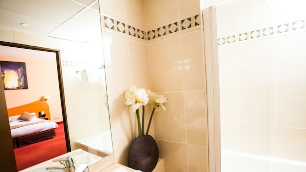 Une salle de bain d’hôtel avec un grand miroir, un lavabo, une baignoire et un vase rempli de fleurs.