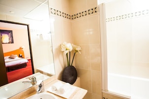 Un baño de hotel con un espejo grande, un lavabo, una bañera y un florero con flores.