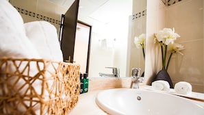 Une salle de bain avec un lavabo blanc, un panier en osier, un miroir et un vase rempli de fleurs.