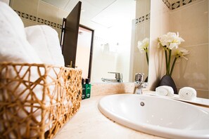 Un baño con lavamanos blanco, una cesta de mimbre, un espejo y un florero con flores.