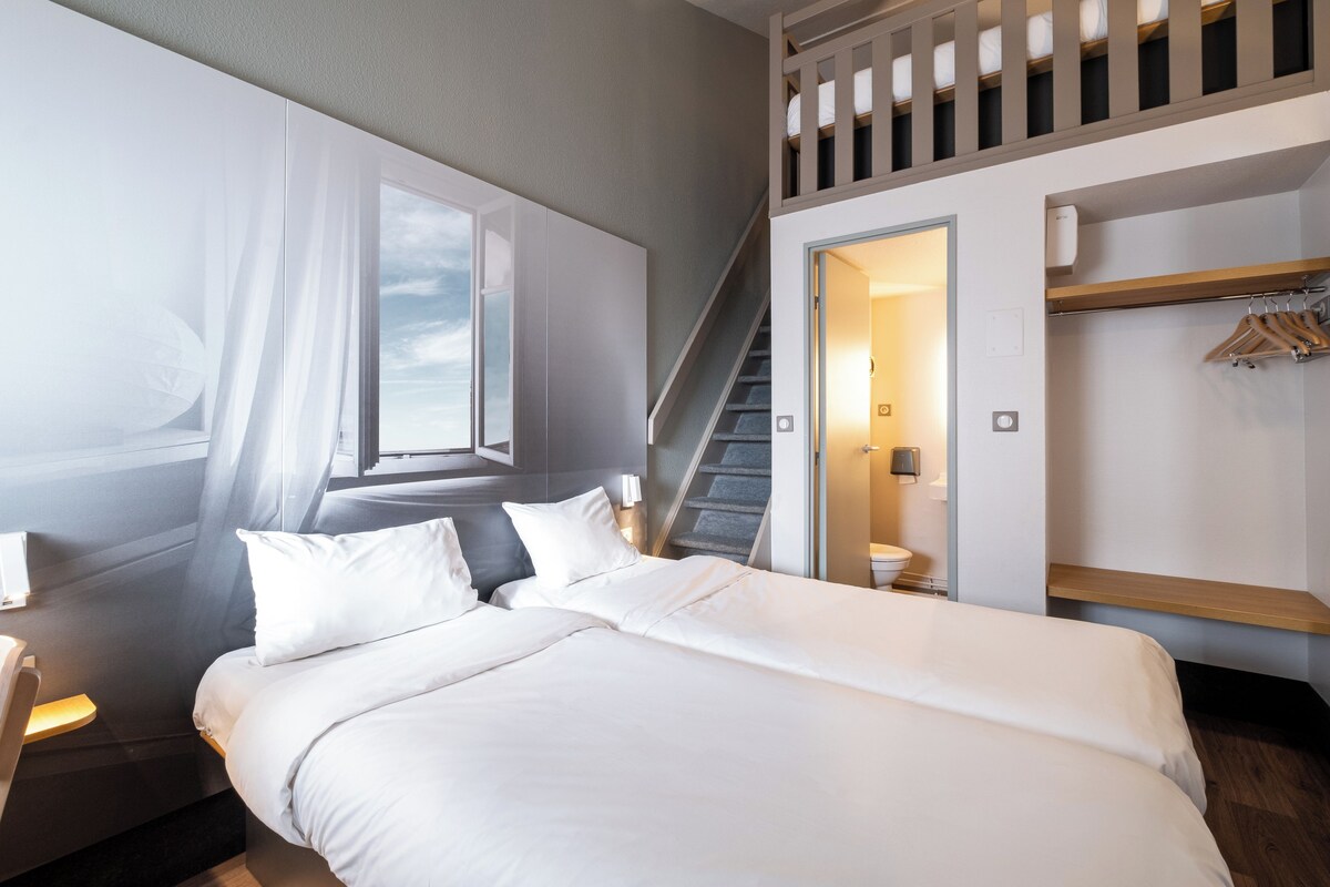A modern hotel room with a large bed, a staircase, and a wardrobe with hanging clothes.
