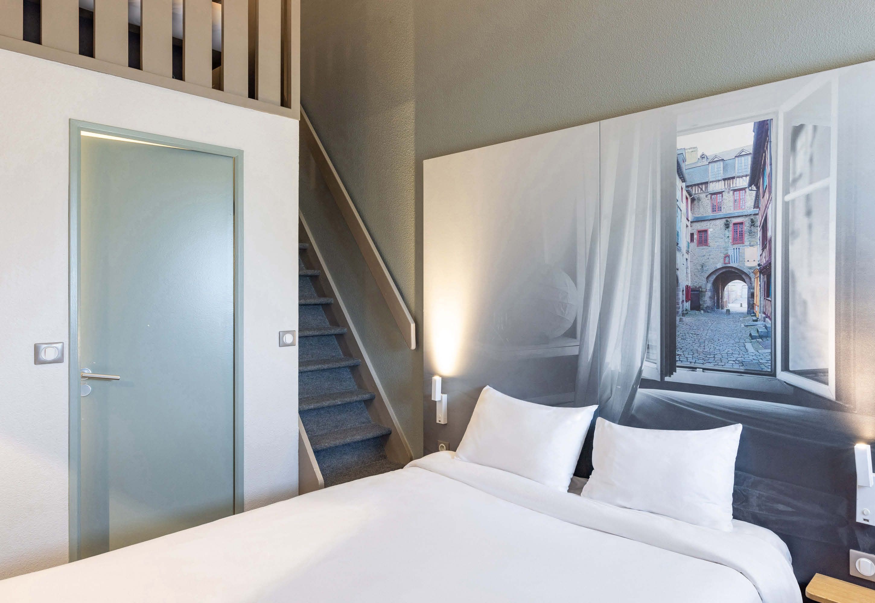 A hotel room with a bed, a staircase, and a mural of a street scene.