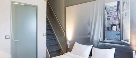Habitación de hotel con una cama, una escalera y un mural de una escena callejera.