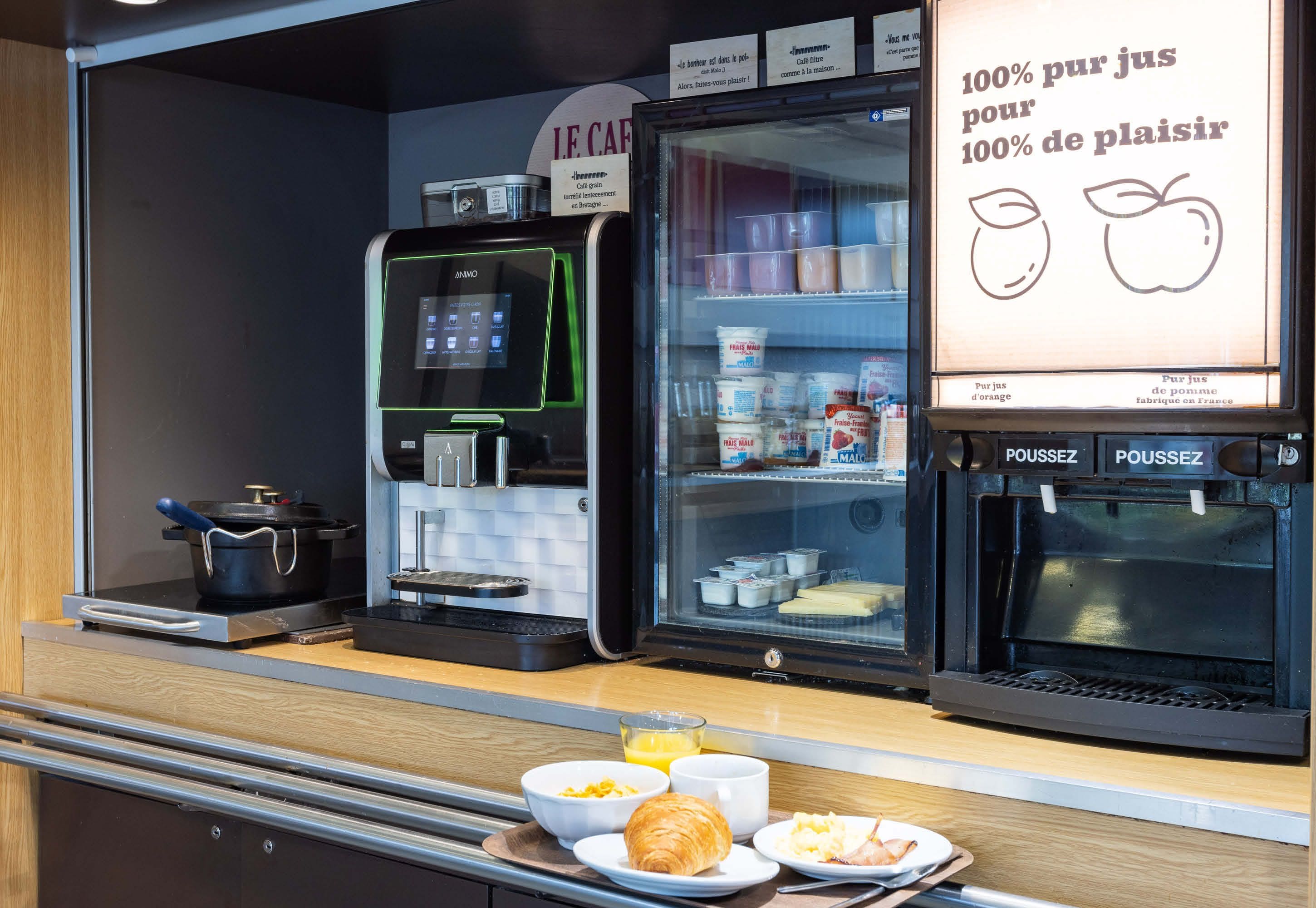 A breakfast counter with a coffee machine, a refrigerator with dairy products, and a sign advertising 100% pure juice.