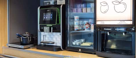 A breakfast counter with a coffee machine, a refrigerator with dairy products, and a sign advertising 100% pure juice.