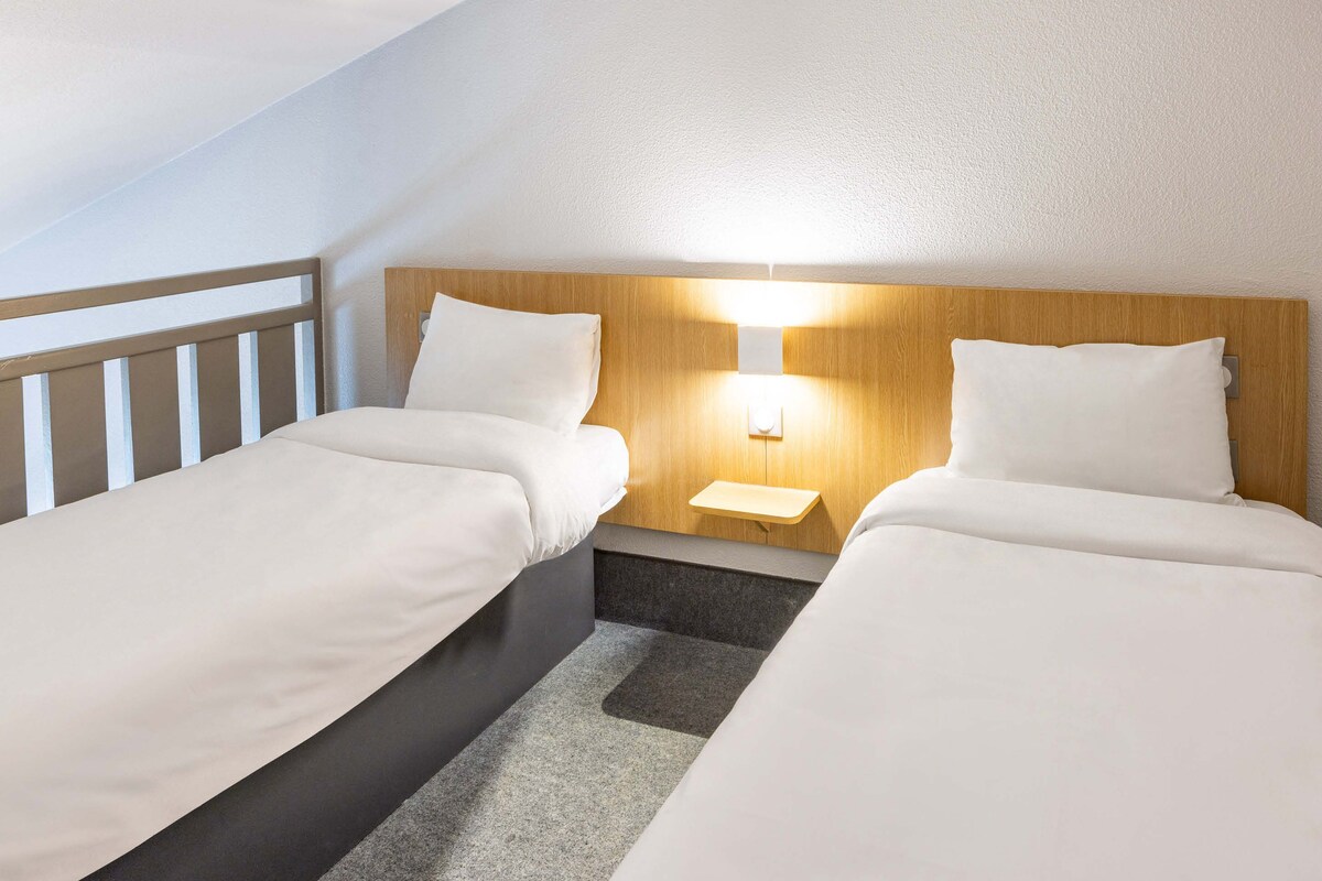 A hotel room with two single beds, a nightstand with a lamp, and a wooden headboard.