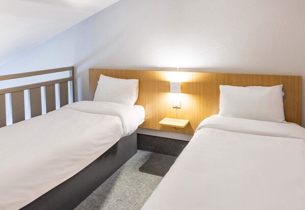 A hotel room with two single beds, a nightstand with a lamp, and a wooden headboard. - B&B Hotel Rennes Nord St Gregoire (Saint-Gregoire)
