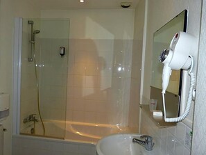 Un baño con ducha de mampara de vidrio, un lavamanos blanco y un secador de pelo montado en la pared.