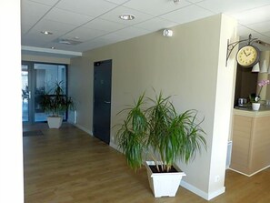 Un couloir avec un plancher en bois, une plante en pot, une porte et une horloge au mur.
