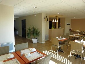 Un'area ristorazione di un hotel con tavoli apparecchiati per la colazione, una pianta in vaso e un orologio appeso al muro.