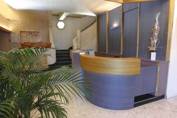 A reception area with a curved desk, a staircase, and a potted plant. - Du Berry (Saint-Nazaire)