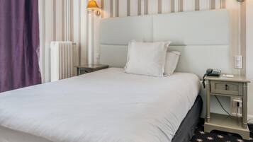 Une chambre d’hôtel avec un grand lit, deux tables de chevet, une tête de lit et une fenêtre avec des rideaux.