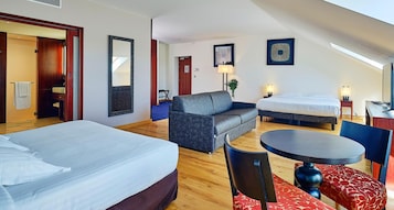 Habitación de hotel con cama, sofá, mesa de comedor y una pequeña cocina.