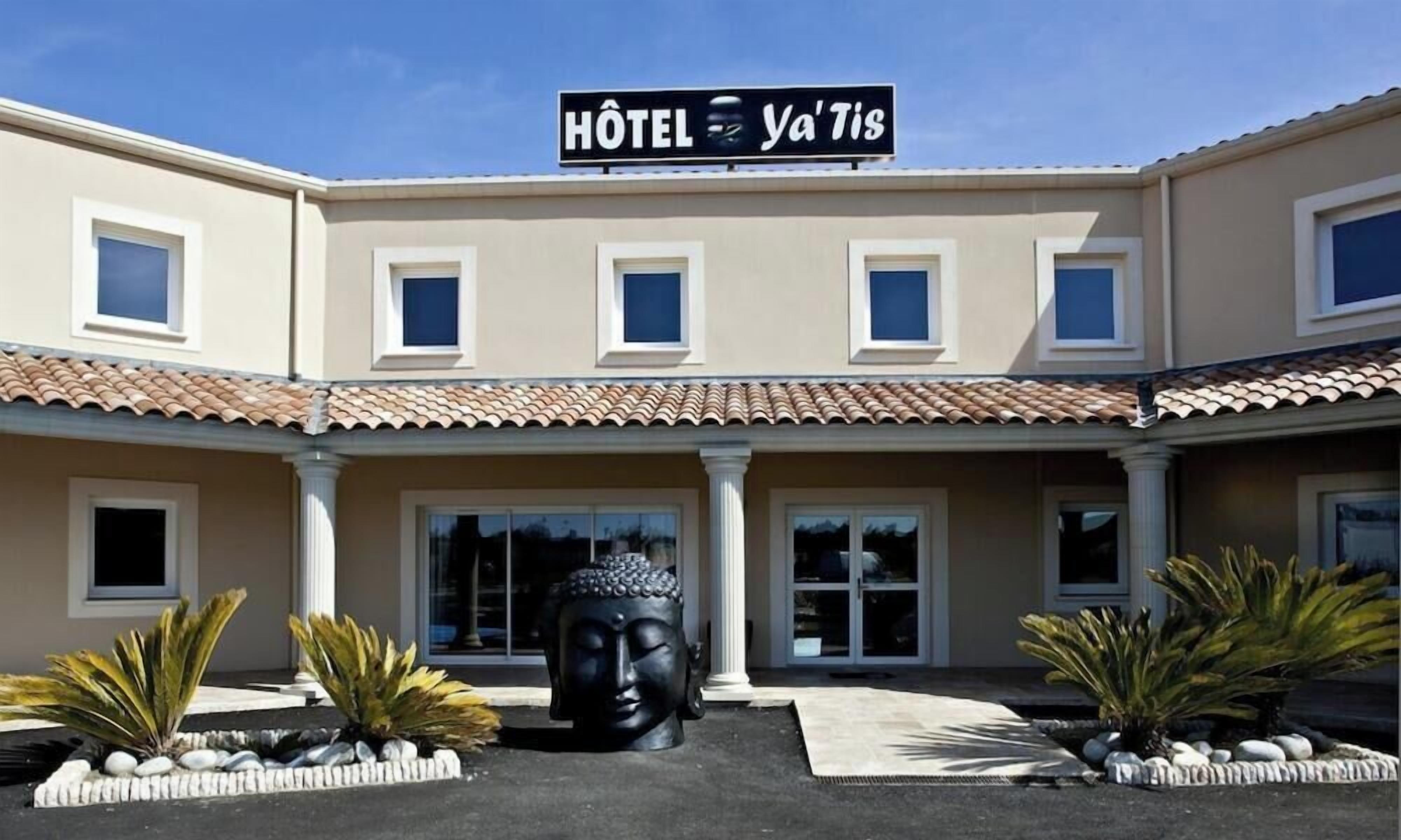 A hotel with a sign reading "Hôtel Ya'Tis" and a Buddha statue in front.