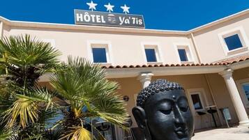 A building with a sign reading "HOTEL Ya'Tis" and a Buddha statue in front.
