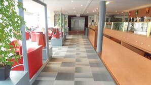 A hotel lobby with a check-in counter, red seating area, and a patterned floor. - Club Belambra Le Normont (Dourdan)