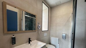 Een moderne badkamer met een wit wastafelmeubel, een spiegel, toilet en een douche.