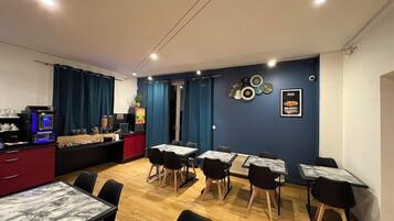 Un espace repas avec des tables et des chaises, une machine à café et un comptoir où est affiché le menu.