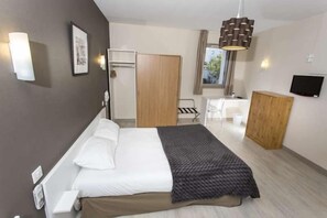 Una habitación de hotel con cama, escritorio, silla, armario y televisor.