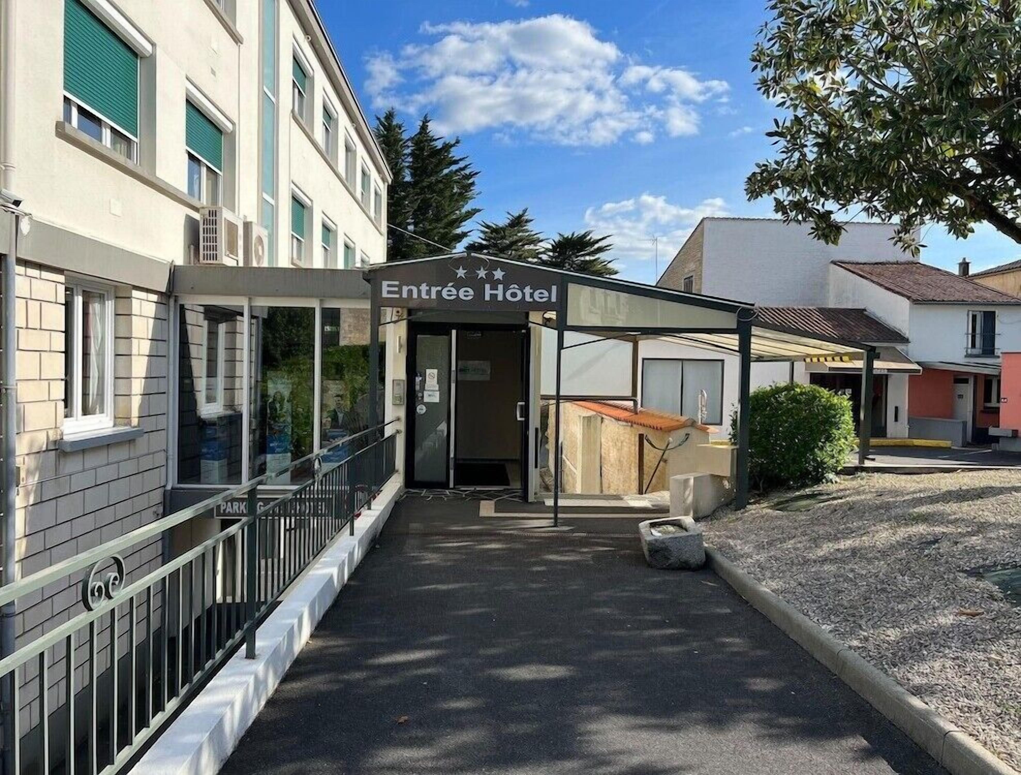 L’entrée d’un hôtel, avec un espace d’attente abrité, un panneau indiquant clairement l’emplacement du parking et un ciel dégagé.