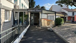 Een hotelingang met een overdekte wachtruimte, een zichtbaar parkeersbord en een heldere lucht.