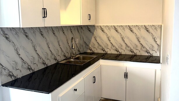 A kitchen with white cabinets, a black countertop, and a marble backsplash. - Ranisa (Kampot)