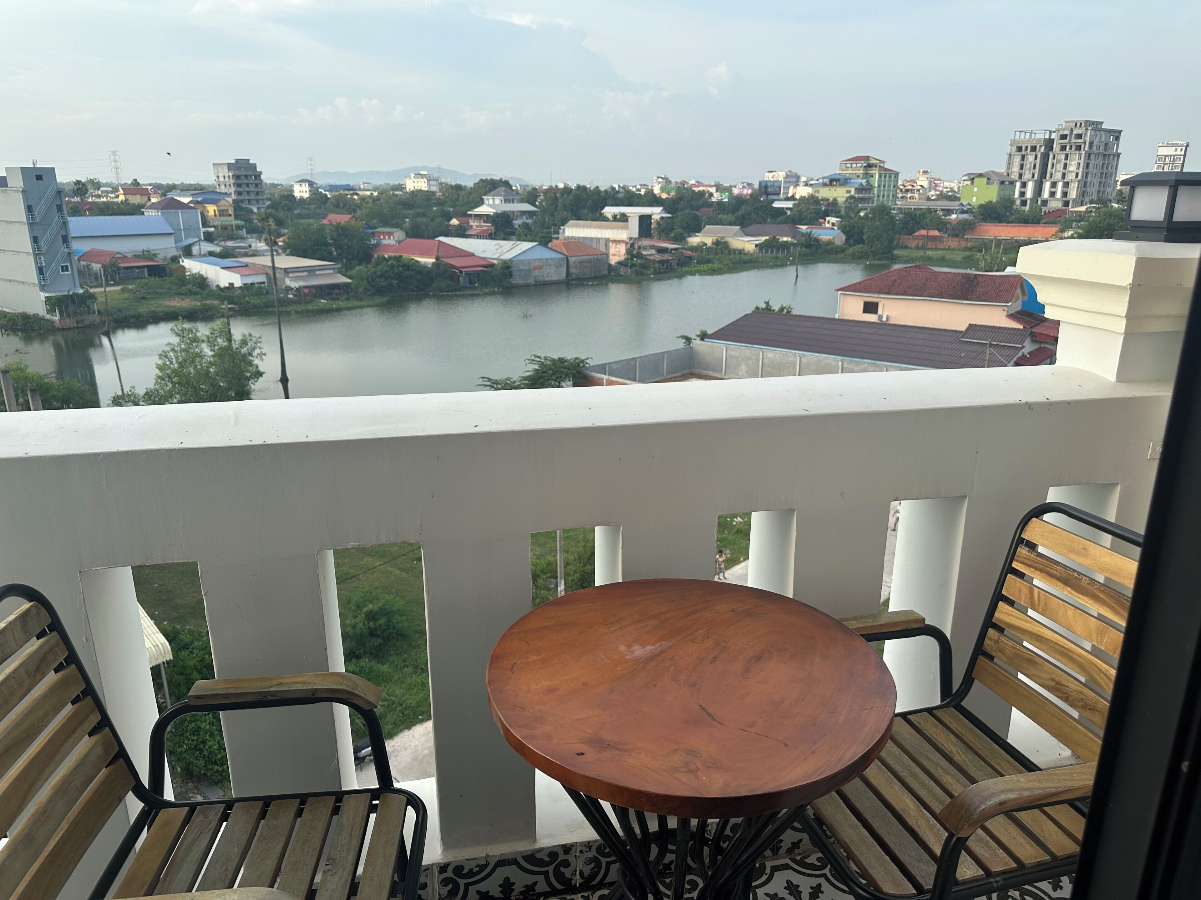 A balcony with a table and chairs, overlooking a river with buildings in the background.