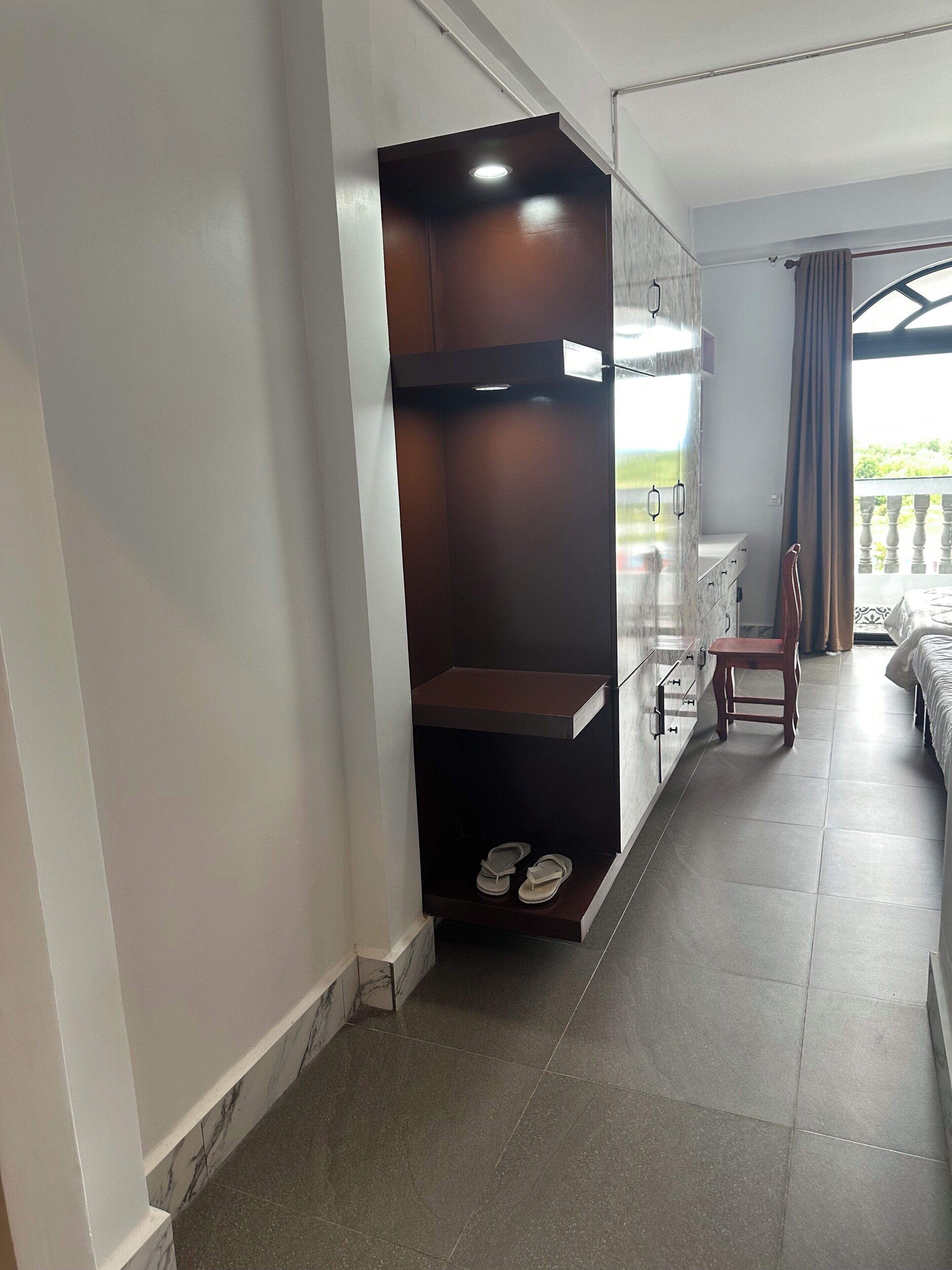 A hotel room with a bed, a small table, a chair, a wardrobe, and a view of the outdoors.