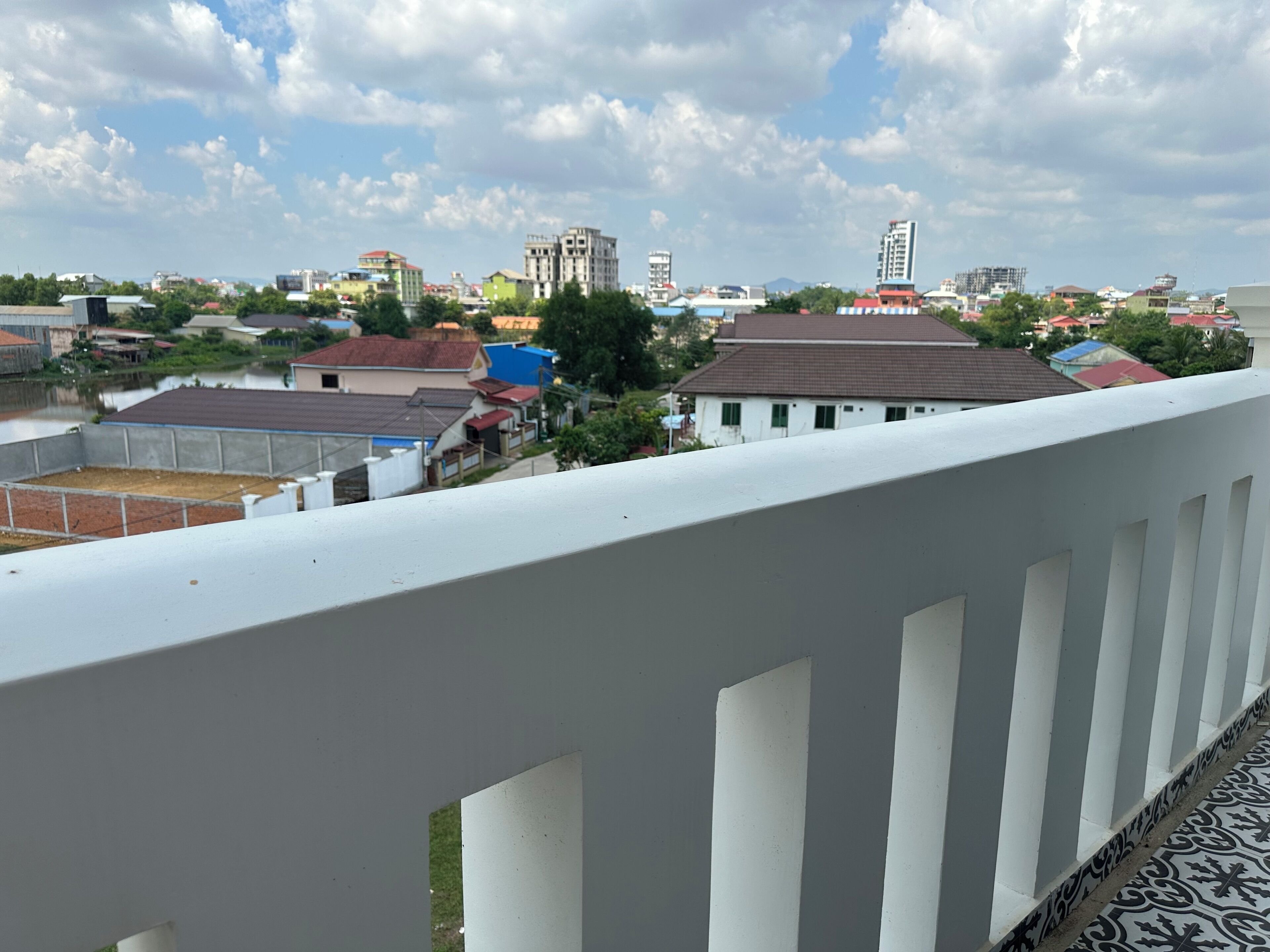 A balcony with a white railing overlooking a residential area with various buildings and a clear sky.