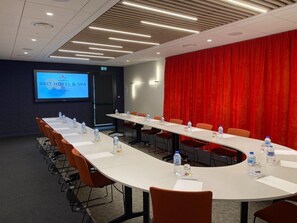 A conference room with a long table, orange chairs, and a red curtain backdrop. A screen displays "BRIT HOTEL & SPA". - Brit Hotel Fougeres - Hotel Du Parc (Lecousse)